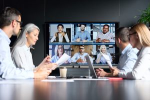 A group of professionals from the staffing industry are on a Zoom call, sitting at their desks with laptops open in front of them. The participants are seen in various positions, some are smiling and engaged in conversation, while others are taking notes or listening attentively. The background is a mix of home offices and professional settings, with bookshelves, artwork, and office equipment visible in some of the participants' video feeds. The overall tone of the image is one of collaboration, professionalism, and focused discussion